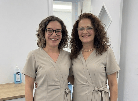 Dos profesionales sanitarias de la clínica dental y de medicina estética en Santomera, Murcia, sonriendo con uniforme médico beige tipo pijama en el interior de la consulta.